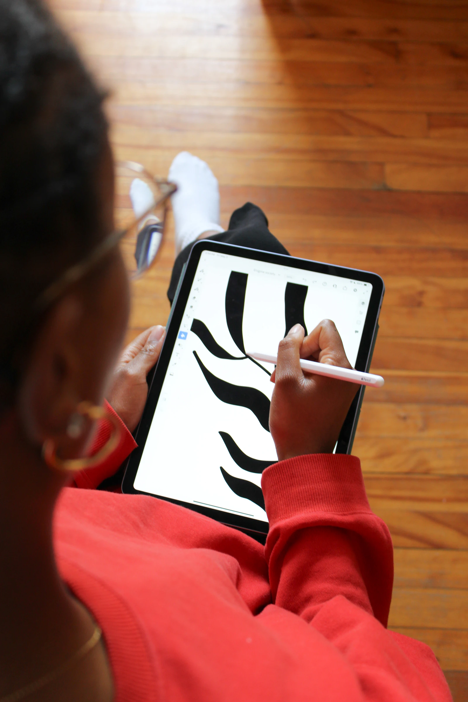 A person in a red sweater drawing black shapes on a tablet